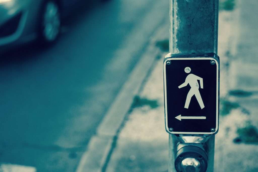 A pedestrian crossing button on a street pole with a symbol of a person walking, indicating a crosswalk nearby.